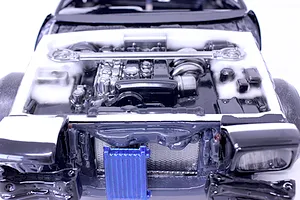 Detailed model car engine bay insert installed in a chassis, featuring a painted engine block, strut bar, and radiator against a white background.