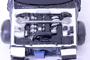 Top-down view of a detailed model car engine bay featuring a painted engine block, strut bar, and components inside a white chassis.