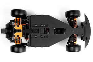 Top-down studio view of an RC car chassis showcasing its black deck, black rubber wheels, and bright orange aluminum suspension mounts against a plain white background.