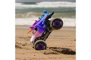 Losi Mini LMT Sparkle Smash RC monster truck performing a vertical wheelie on a sandy beach with ocean waves in the background.