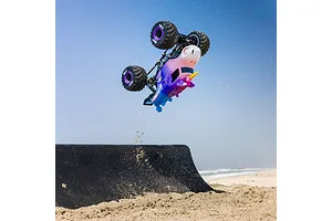 Losi Mini LMT Sparkle Smash RC monster truck jumping high in the air off a ramp on a sandy beach.