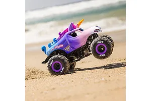 Losi Mini LMT Sparkle Smash RC monster truck driving on a sandy beach with ocean waves in the background.