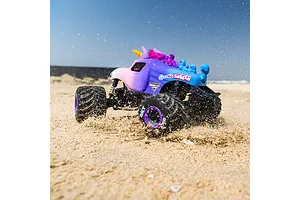 Losi Sparkle Smash RC monster truck kicking up sand on a beach under a blue sky.