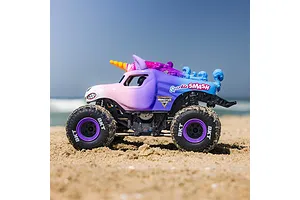 Losi Mini LMT Sparkle Smash RC Monster Truck driving on a sandy beach under a clear blue sky.