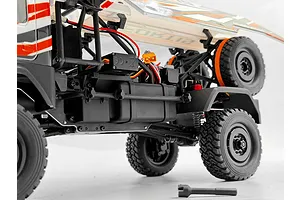Close-up side view of the HobbyPlus DKR-4 Fortis RC truck chassis, showing internal electronics, roll cage, and spare tire against a white background.