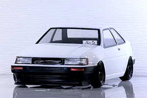 Front three-quarter view of a white Toyota AE86 Corolla Levin RC drift car body with black wheels on a reflective surface.