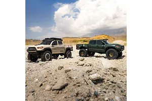 Two Axial SCX30 Toyota Tacoma RC rock crawlers in tan and green driving on rocky outdoor terrain.