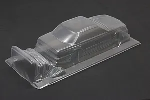 Unpainted clear polycarbonate RC drift car body shell sitting on a dark surface, showing the sedan profile.