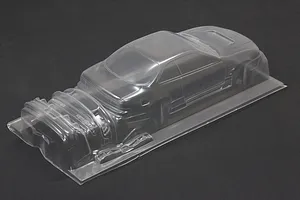 Unpainted clear polycarbonate RC drift car body shell with separate bumper and part moldings set against a dark background.