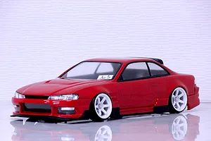 A painted red RC drift car body shell mounted on a chassis with white wheels against a white background.