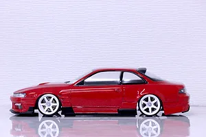 Side profile view of a red RC drift car body on a reflective surface against a white textured background.