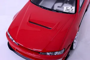 Close-up of the red hood and front section of a painted RC drift car body with a white decal on the windshield.