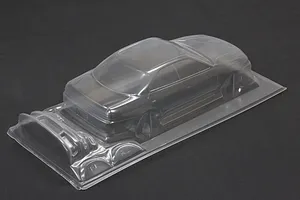 Unpainted clear polycarbonate RC drift car body shell with additional molded parts on a dark background.