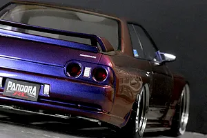Rear three-quarter view of a painted Pandora RC BNR32 Skyline GT-R body shell showing iridescent purple and bronze paint, rear spoiler, and custom license plate.