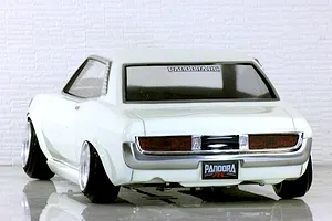 Rear three-quarter view of a white Pandora RC Toyota Celica 1600GT drift car body shell on a reflective surface with a brick wall backdrop.