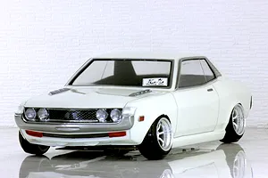 A painted white Toyota Celica 1600GT 7800 RC drift car body shell mounted on a chassis with custom wheels against a brick background.