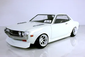 Front three-quarter view of a white Toyota Celica 1600GT RC body shell mounted on a chassis with custom wheels against a white background.