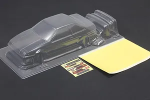 Unpainted clear polycarbonate RC car body shell with additional molded parts, window masks, and decal sheet on a dark surface.