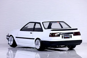 Rear three-quarter view of a white RC drift car body shell modeled after a Toyota AE86 Trueno, featuring custom wheels and black trim.