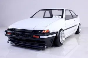 Front three-quarter view of a white RC drift car body shell modelled after a Toyota AE86 Trueno with black trim and custom wheels.
