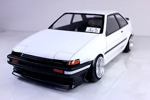 Front three-quarter view of a white Pandora RC Toyota AE86 Sprinter Trueno 2-door drift car body shell with black trim and deep dish wheels.