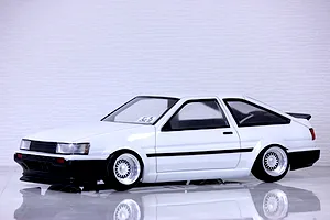 A painted white Toyota AE86 Corolla Levin 3-door RC body shell mounted on a chassis with wire-mesh wheels, sitting on a reflective surface.