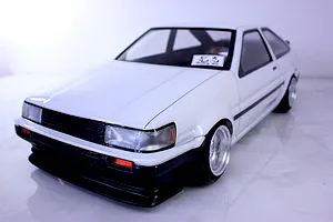 Front three-quarter view of a painted white Toyota AE86 Corolla Levin RC drift car body shell mounted on a chassis.