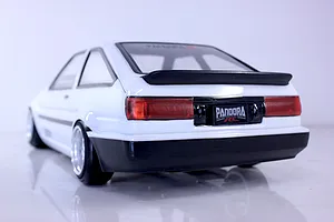 Rear-three-quarter view of a painted white Toyota AE86 Corolla Levin RC drift car body shell with black bumpers and rear spoiler.