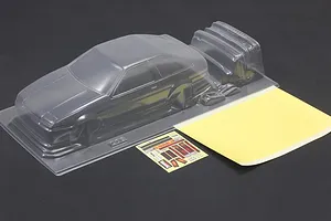 Unpainted clear polycarbonate RC car body shell with additional molded parts, a sticker sheet, and masking paper on a dark surface.