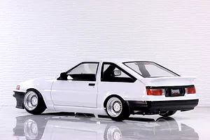 Rear-three-quarter profile view of a white Toyota AE86 Sprinter Trueno RC drift car body on a reflective white studio surface.