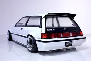 Rear-three-quarter view of a white RC Honda Civic Si body shell mounted on a chassis with custom wheels against a white studio background.