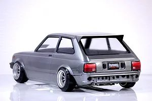 Rear-three-quarter view of a painted grey Toyota Starlet KP61 RC drift car body shell with Pandora RC license plate and custom wheels on a reflective white surface.