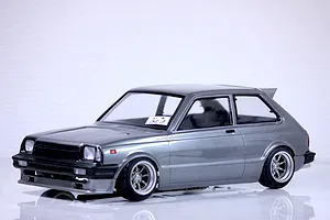 A painted grey Toyota Starlet KP61 RC drift car body shell mounted on a chassis with custom wheels against a white background.
