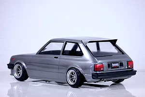 Rear-three-quarter view of a metallic grey Pandora RC Toyota Starlet KP61 RC drift car body on a reflective surface.