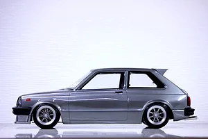 Side profile view of a grey Toyota Starlet KP61 RC body shell mounted on a chassis with wheels against a white background.