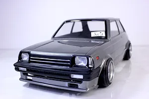 Painted grey RC drift car body shell mounted on a chassis with wheels against a white studio background.