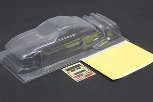 Unpainted clear RC car body shell with separate parts, decal sheet, and masking sheet on a dark surface.