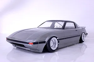 A painted grey Mazda Savanna RX-7 RC drift car body shell mounted on a chassis with white mesh wheels against a white studio background.