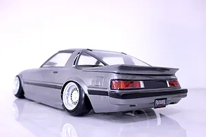Rear three-quarter view of a silver Mazda Savanna RX-7 RC drift car body shell with deep dish wheels on a white background.