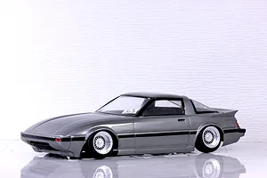 Side profile view of a grey Mazda Savanna RX-7 RC drift car body shell mounted on a chassis with wire-mesh wheels.
