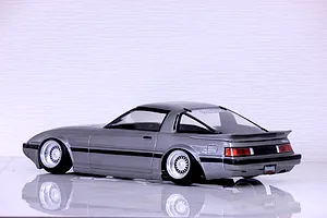 Rear-three-quarter studio view of a silver Mazda Savanna RX-7 SA22C RC drift car body shell on a reflective white surface.
