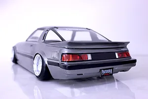 Rear three-quarter view of a grey Mazda Savanna RX-7 RC drift car body shell with deep dish wheels, displayed against a plain white background.