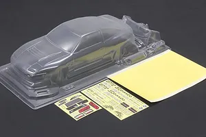 Unpainted clear RC car body shell with separate parts, decal sheets, and mask sheet on a dark surface.