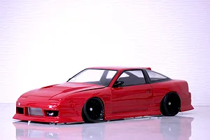 Red RC drift car body shell mounted on a chassis with black multi-spoke wheels on a light surface against a white textured background.