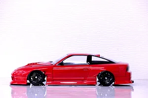 Side profile view of a red RC drift car body shell mounted on a chassis with black wheels against a white background.
