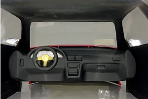 Interior view of an RC car body shell featuring a black dashboard and steering wheel with a gold center.