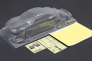 Unpainted clear RC car body shell with separate decal sheets and mask sheets on a dark surface.