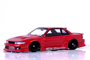 Painted red S13 Silvia drift RC car body shell with BN Sports decals and black multi-spoke wheels on a reflective white studio background.