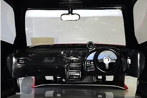 Interior view of an RC car body shell showing a detailed black dashboard, steering wheel, and rearview mirror.