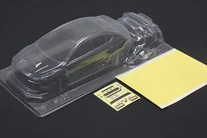 Unpainted clear polycarbonate RC car body shell with a mask sheet and sticker sheet on a dark background.